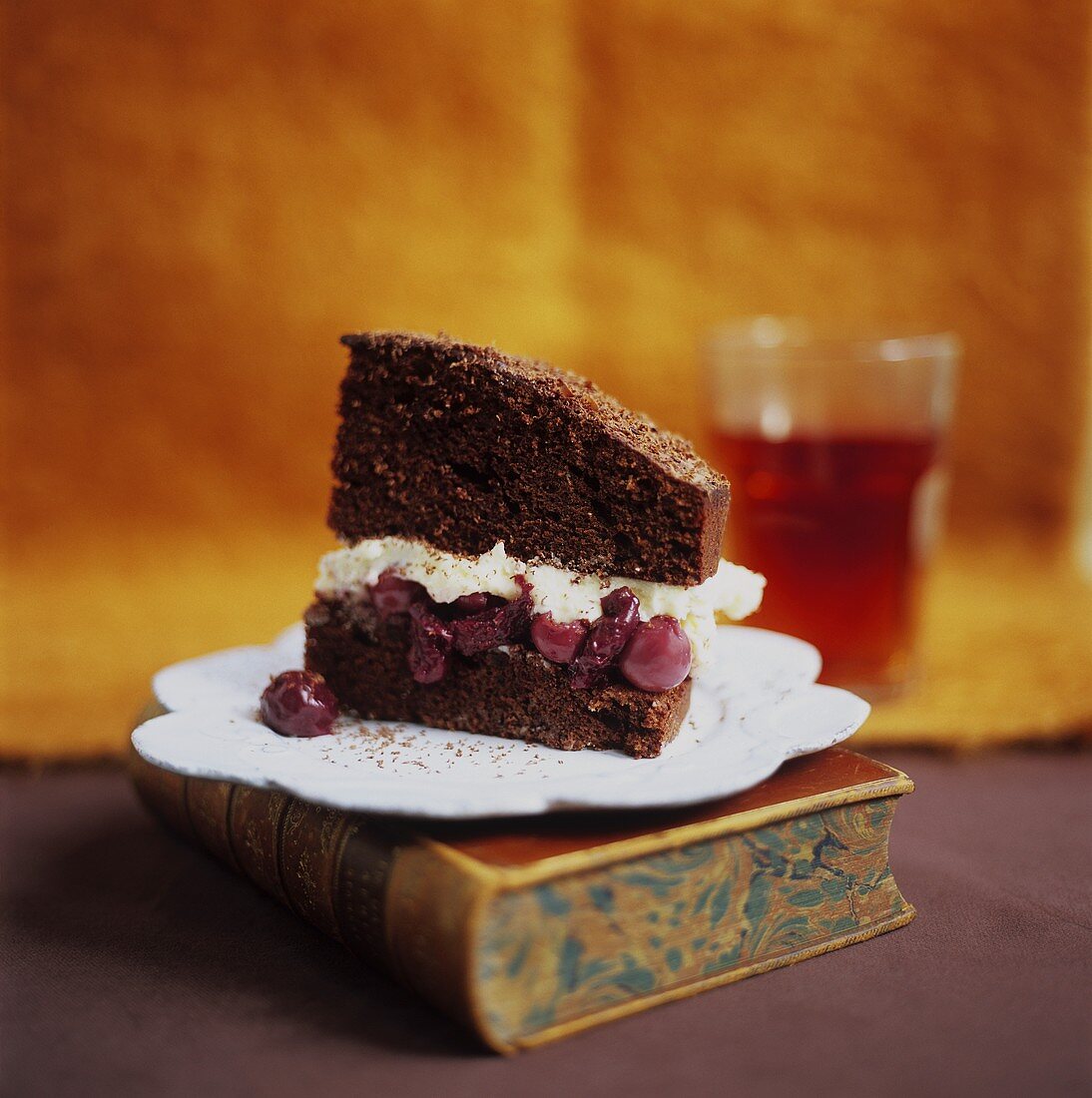 A piece of chocolate cherry cake standing on a book