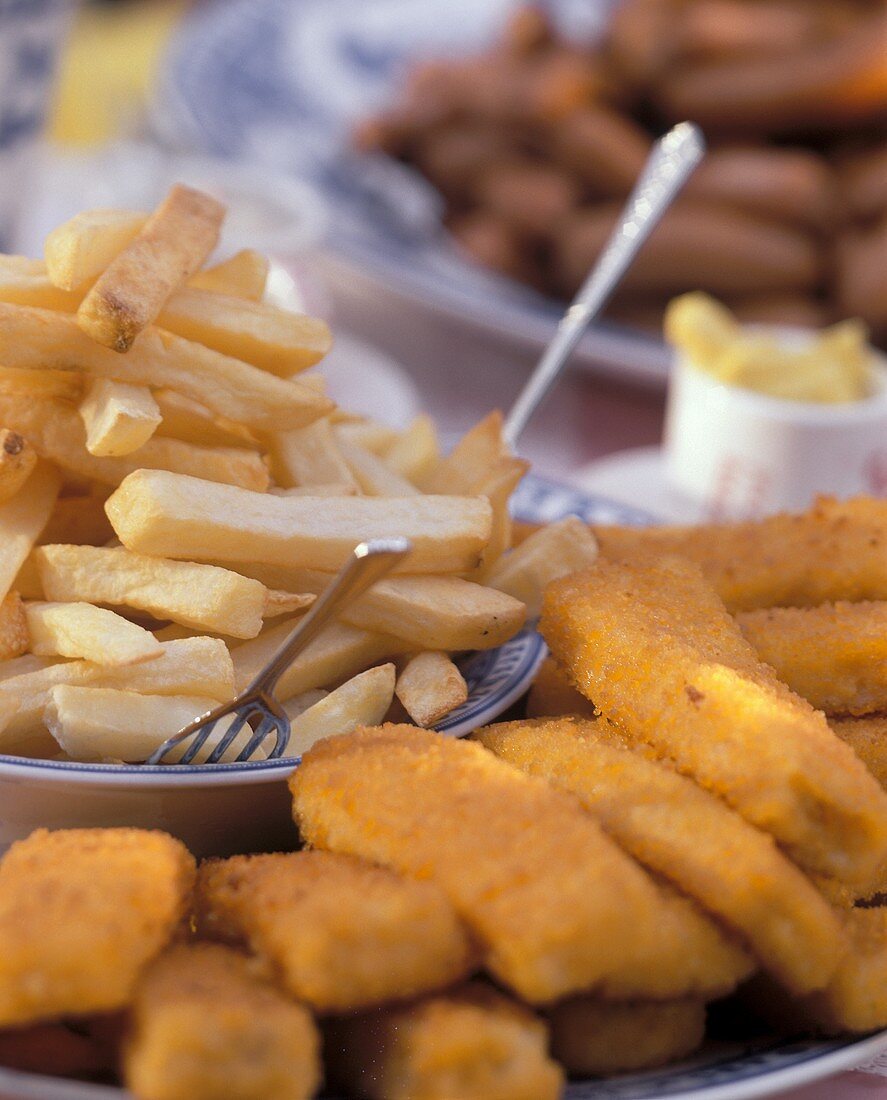 Plate of chips, several fish fingers beside it