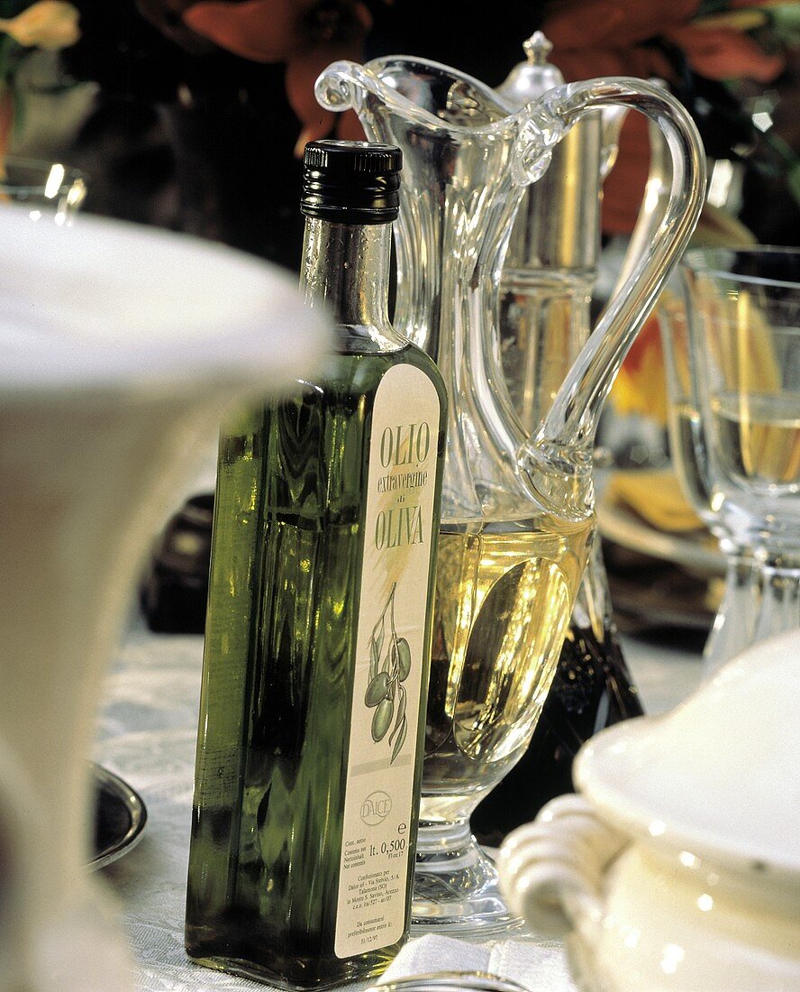 Flasche & Glaskaraffe mit Olivenöl am gedeckten Tisch