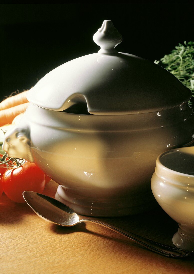weiße Suppenterrine & Löffel, dahinter Tomaten & Möhren
