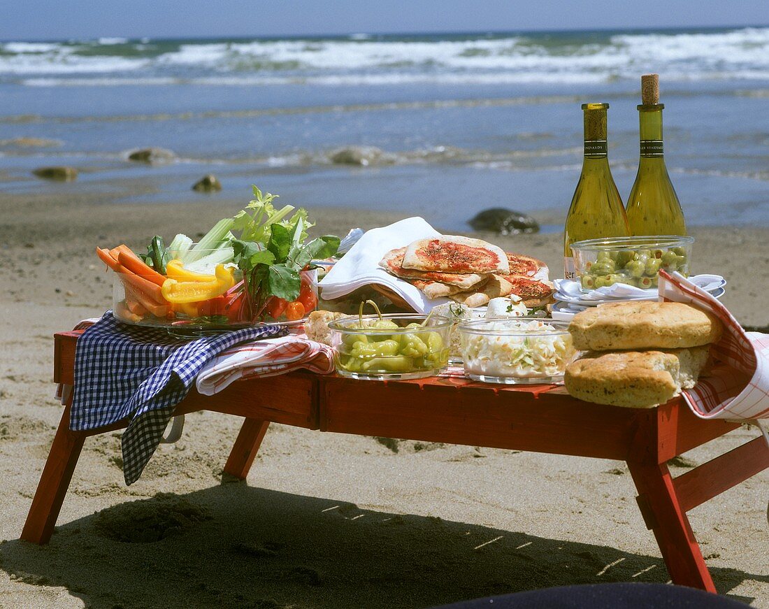 Picknicktisch am Strand mit Pizza, Gemüsesnacks & Wein