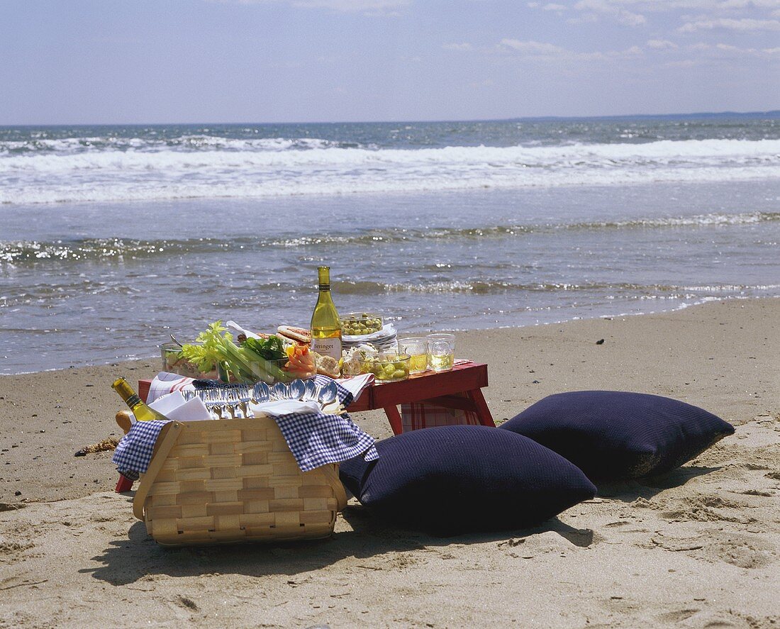 Gedeckter Picknicktisch, Picknickkorb & Sitzpolster am Strand