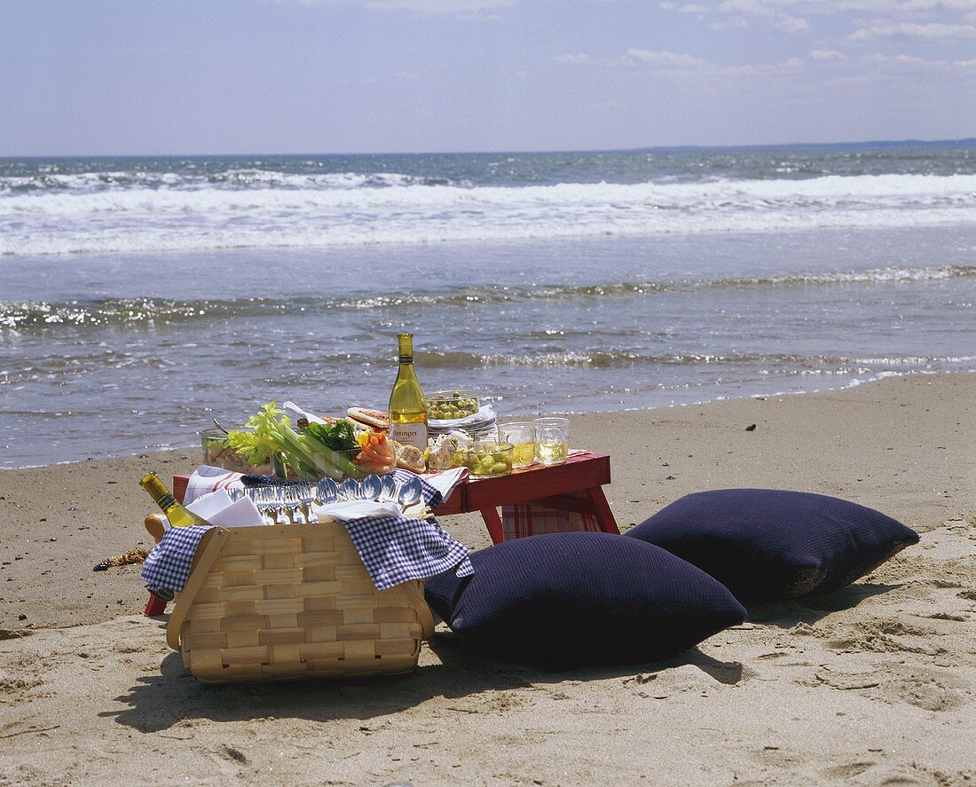 Laid picnic table, picnic basket & cushions on beach