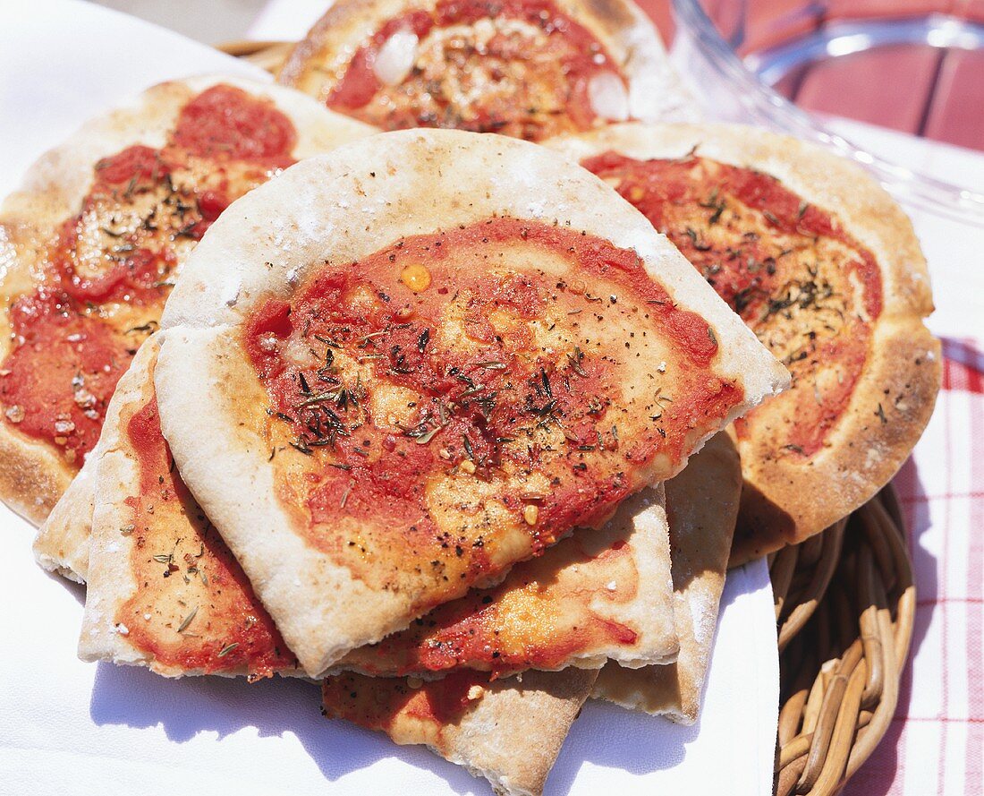 Several pizza breads on wicker tray on picnic table