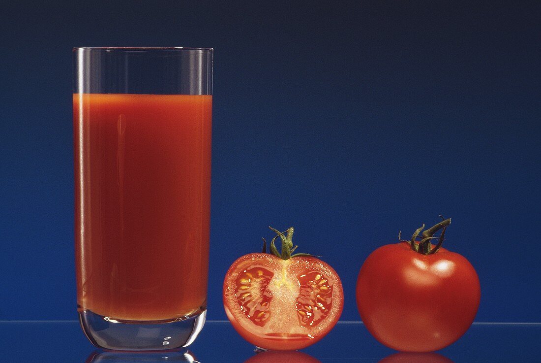 Ein Glas Tomatensaft, daneben eine ganze & halbe Tomate