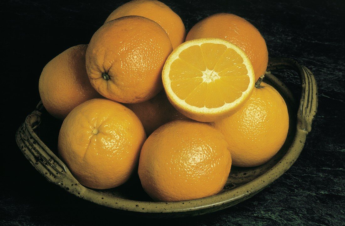 Mehrere ganze Orangen & eine aufgeschnittene auf einem Teller