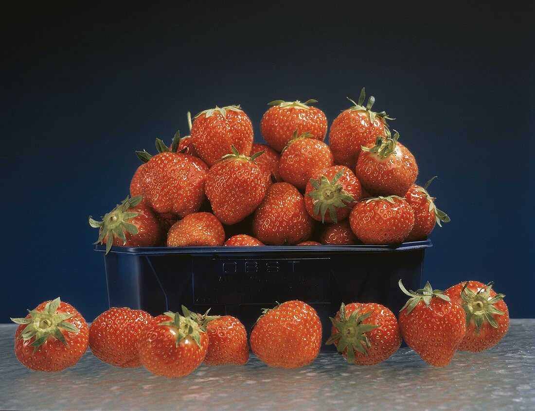 Erdbeeren gehäuft in Plastikschale,davor eine Reihe Erdbeeren