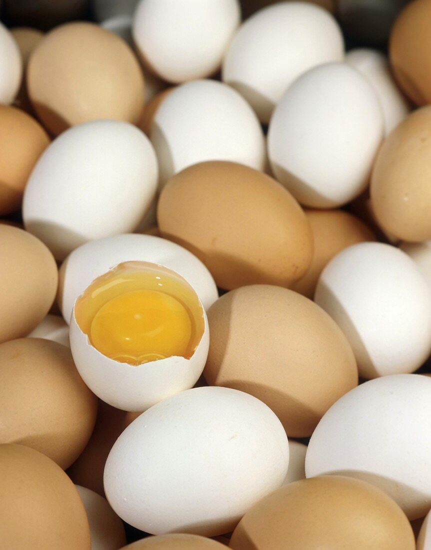 Many brown and white eggs, one broken open