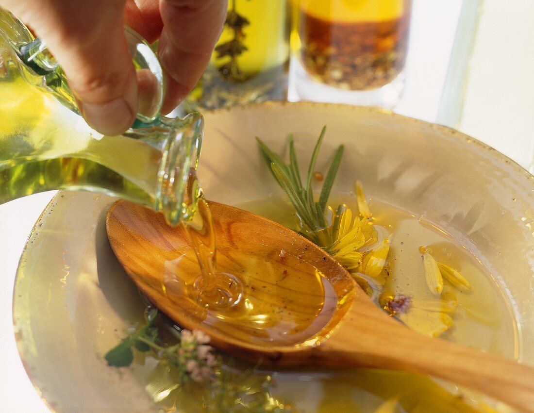 Olivenöl aus Kännchen auf Holzlöffel in Teller gießen