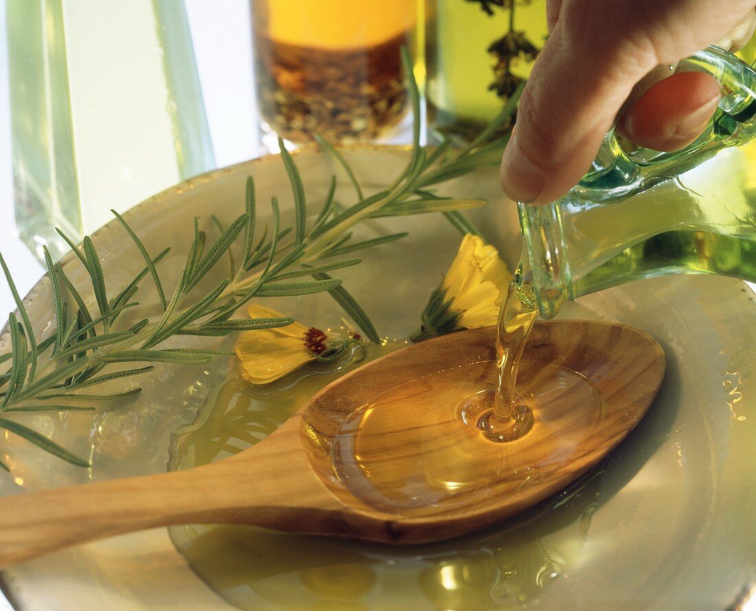 Pouring olive oil out of jug onto wooden spoon on plate