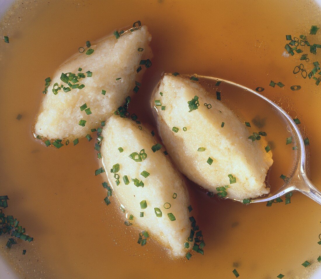 Semolina dumplings (detail) with spoon in broth with chives
