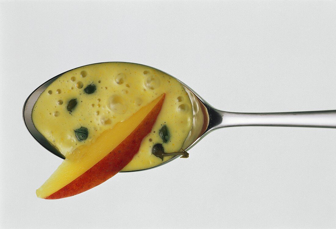 Curried mango sauce with capers & slice of mango on spoon