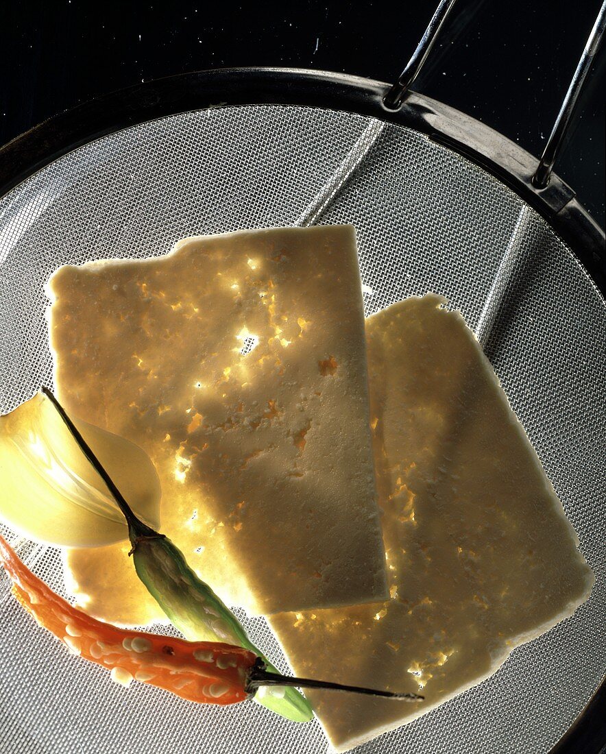 Tofu slices with chili pods and garlic on sieve