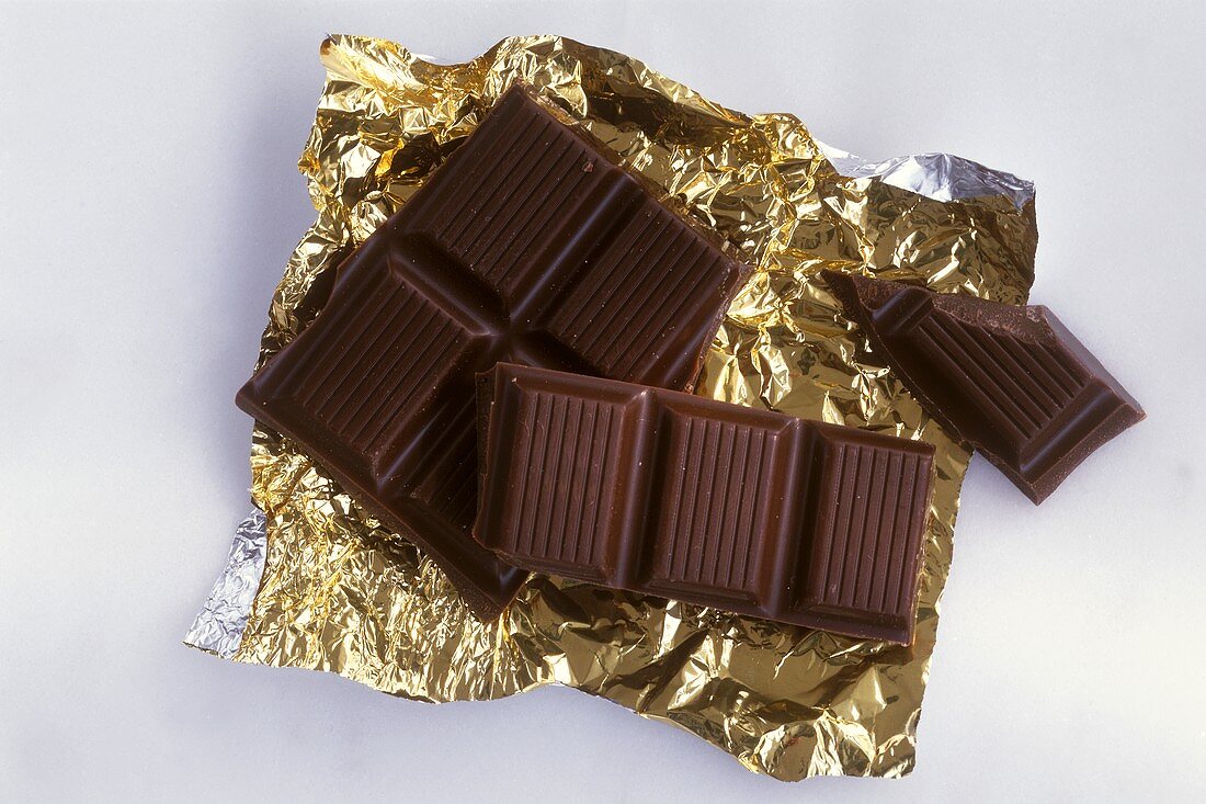 Mehrere Stücke Schokolade auf Goldfolie