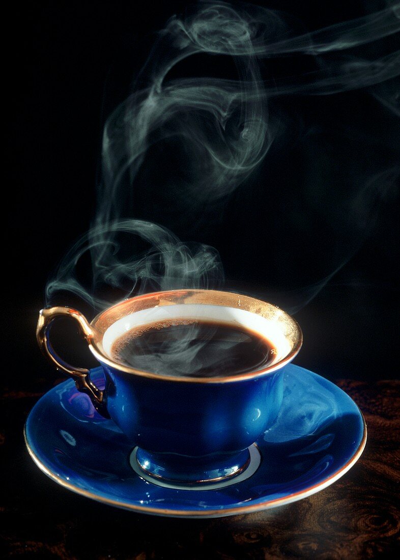 Dampfender schwarzer Kaffee in blauer Tasse mit Goldrand