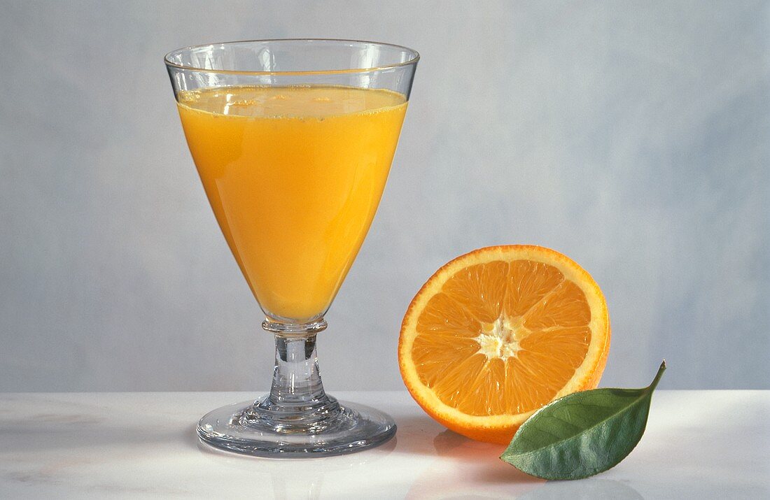 A glass of orange juice, half an orange and a leaf