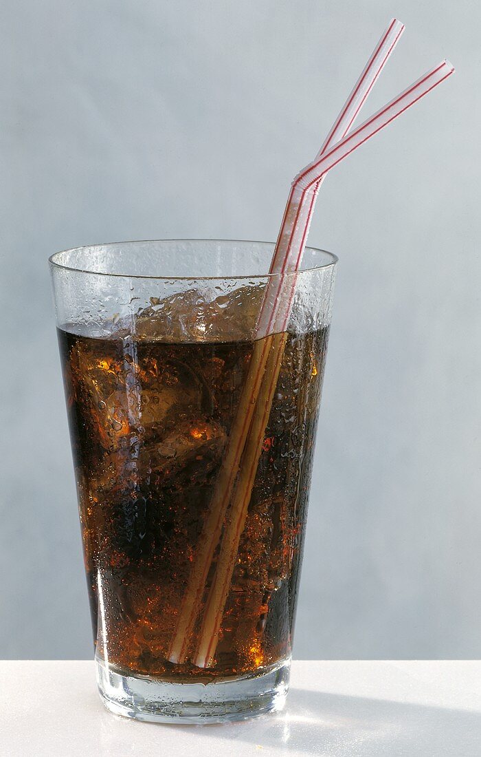 Cola in glass with ice cubes and two straws
