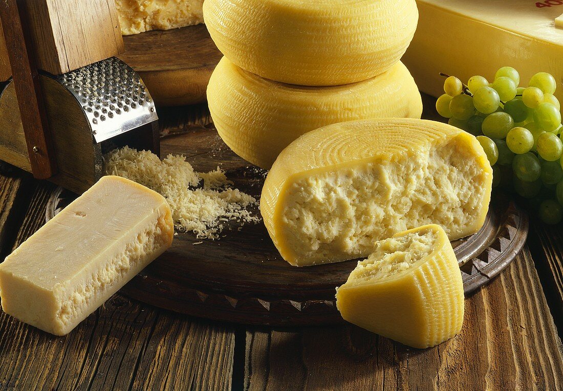 Zwei Käsesorten(Laibe,Stücke) & Käsereibe mit geriebenem Käse