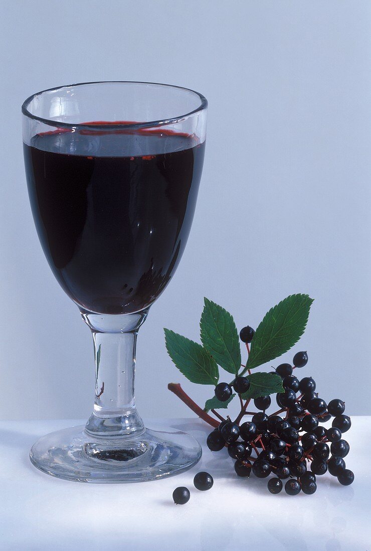 Elderberry juice in glass, a few elderberries beside it
