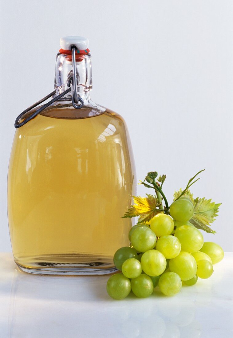 Eine Flasche Weintraubenessig, daneben grüne Trauben
