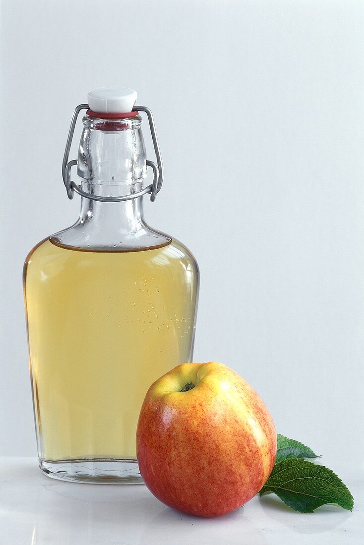 A bottle of apple vinegar and an apple