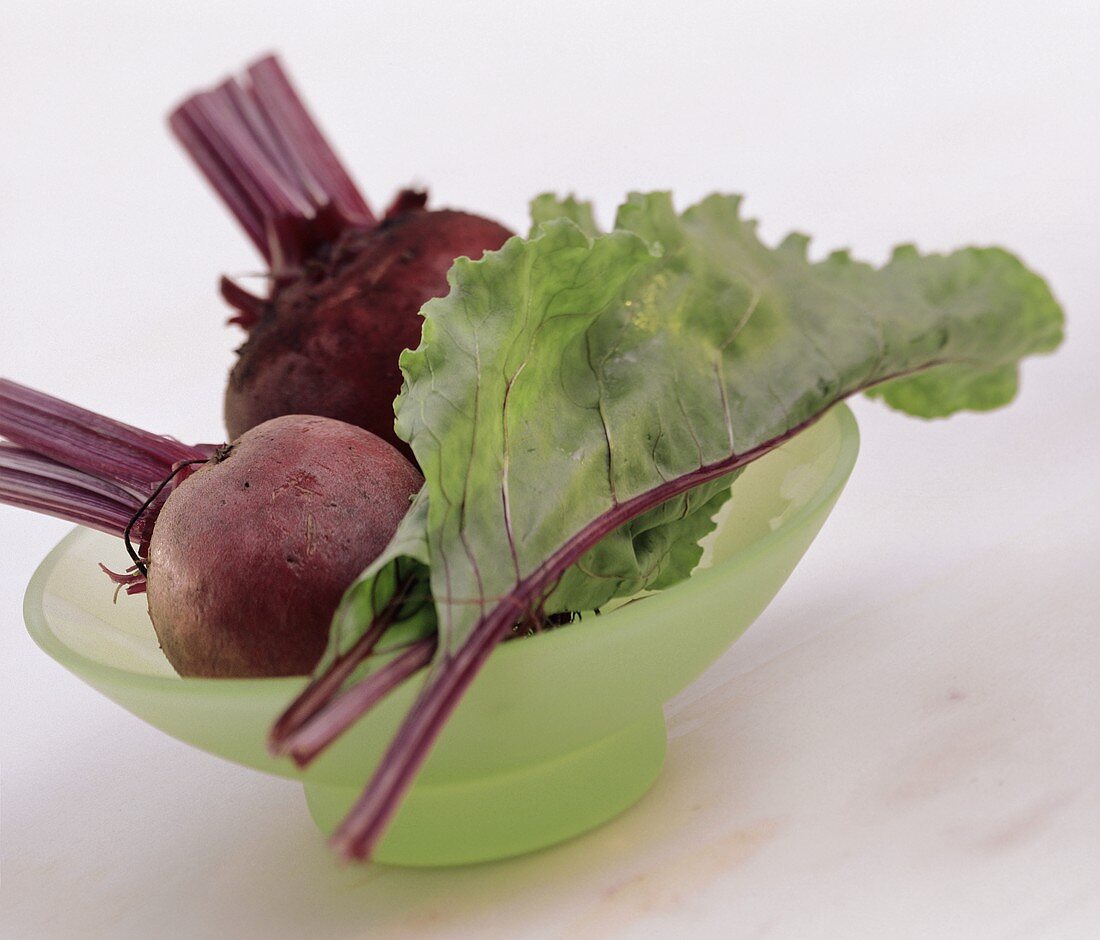 Two beetroots and beetroot leaves in green bowl