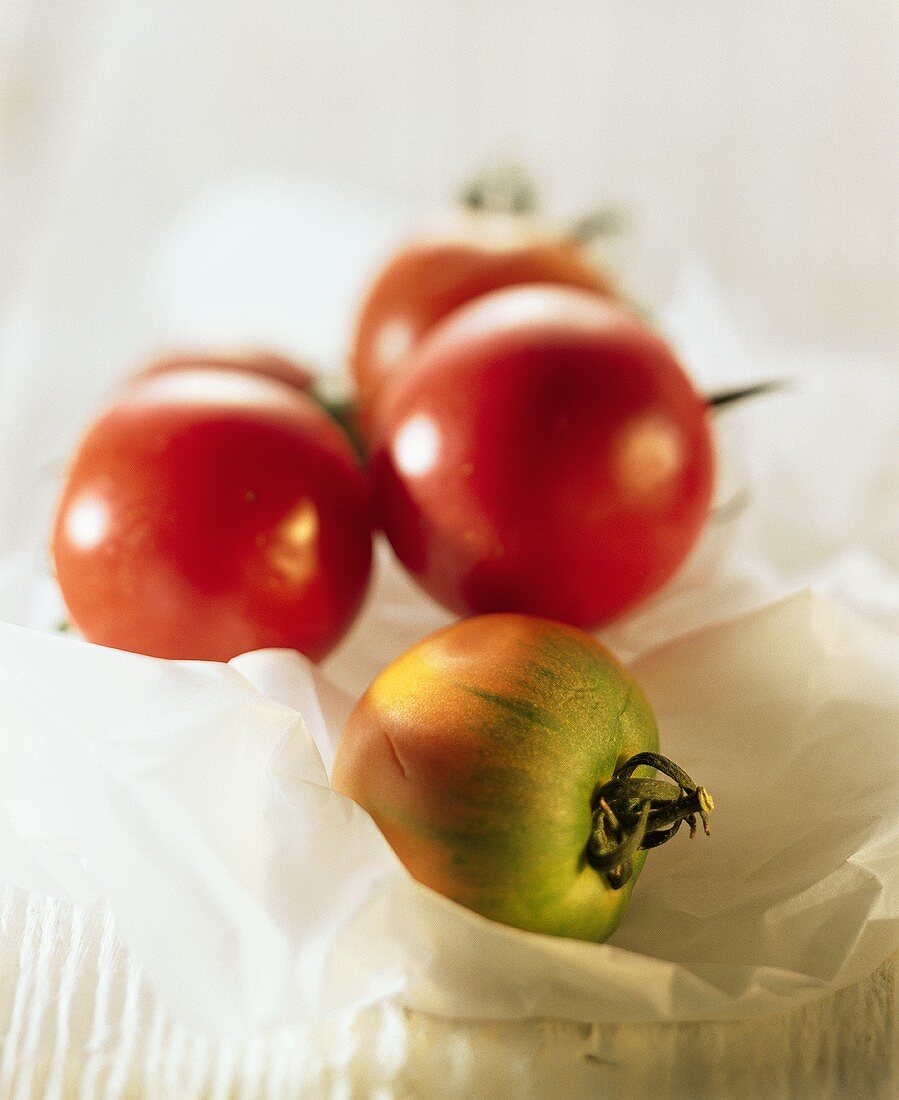 Three ripe tomatoes and one unripe one on white paper