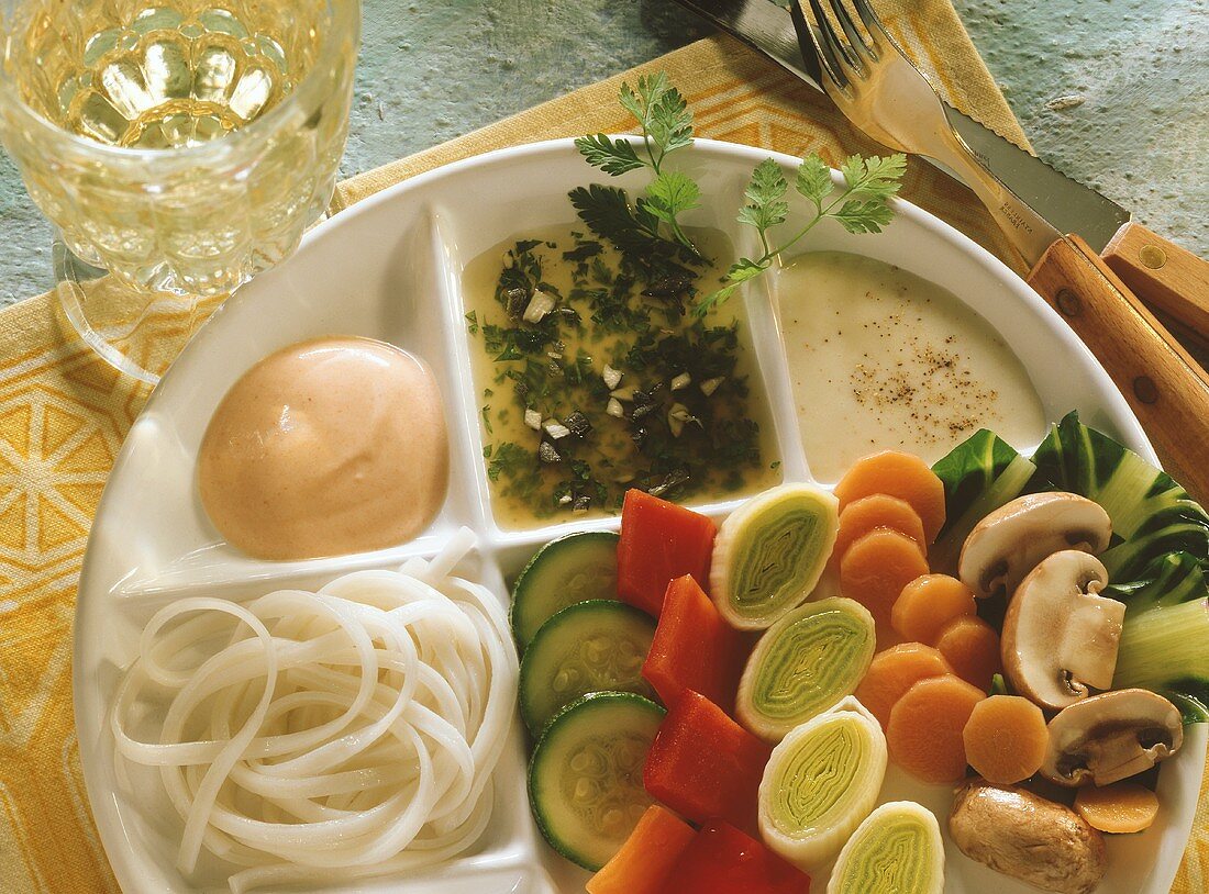Buntes Gemüsefondue mit Reisnudeln und drei Saucen auf Teller