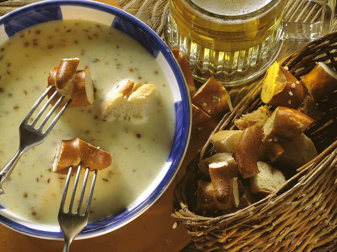 Bier-Käse-Fondue mit Brezenstückchen auf Gabeln und im Korb