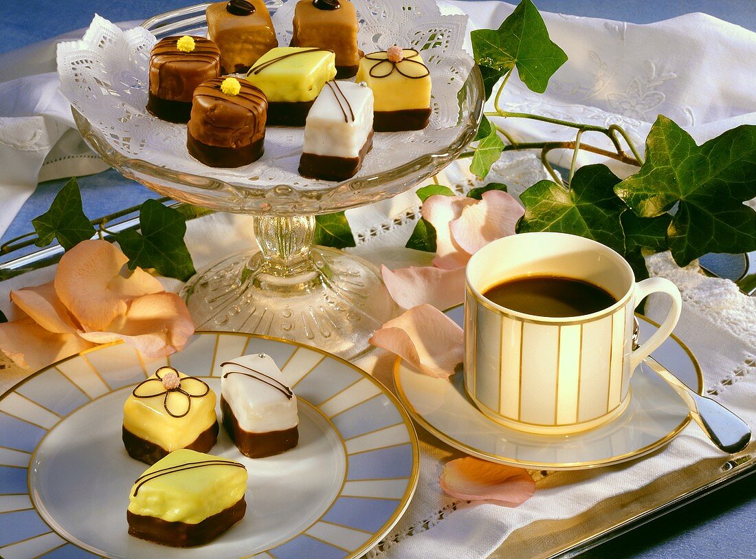 Petit fours auf Teller und Kuchenplatte und eine Tasse Kaffee