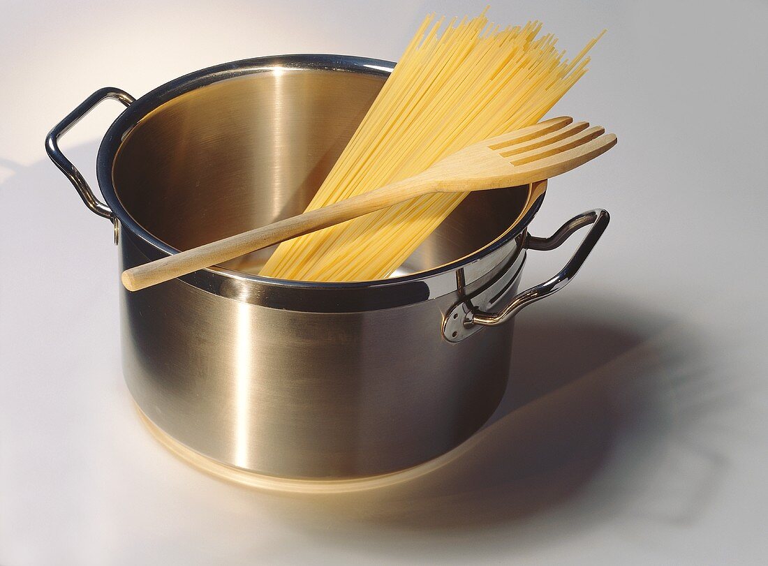 Kochtopf mit Spaghetti und Holzgabel auf hellem Untergrund