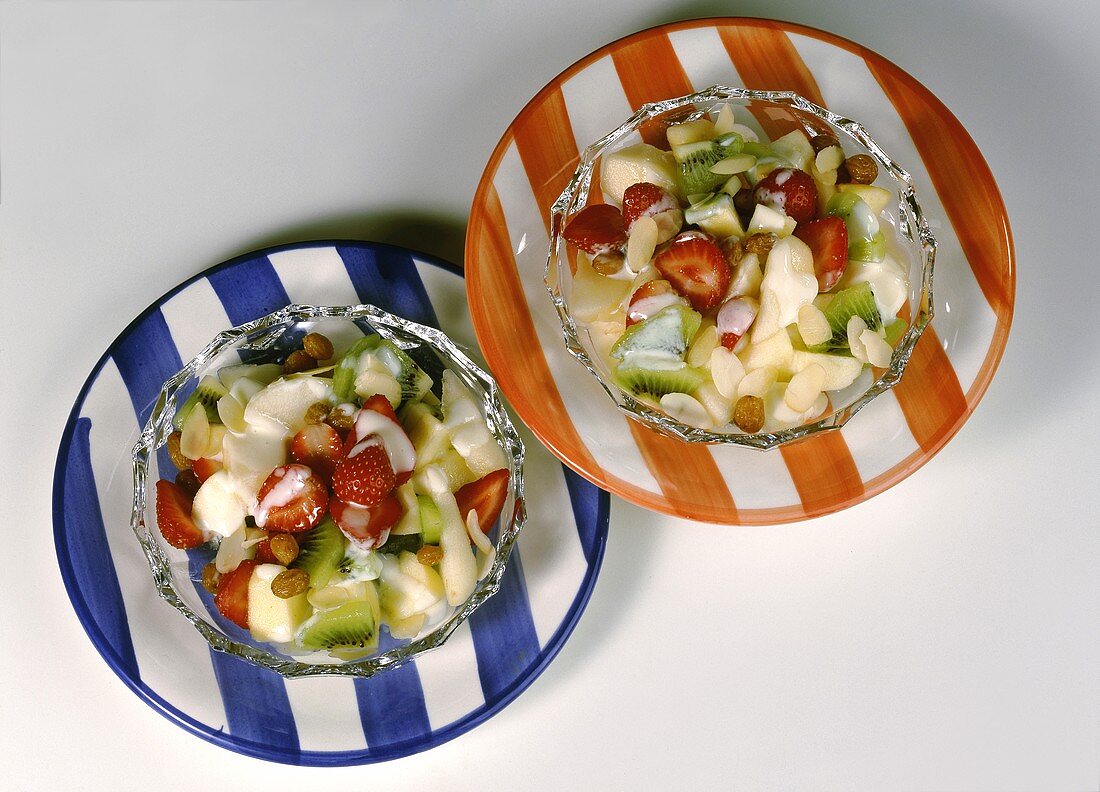 Fruchtsalat mit Joghurt in Glasschälchen auf zwei Tellern