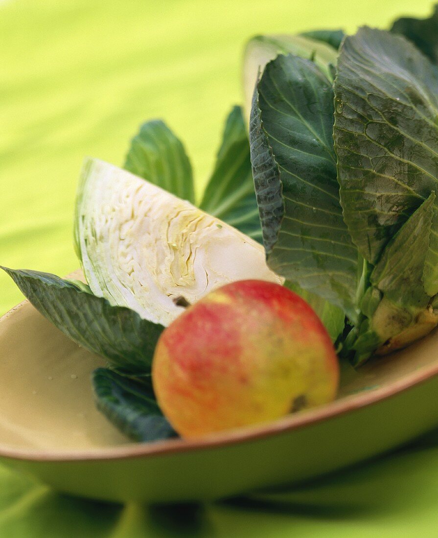 A quarter of a cabbage, cabbage leaves and an apple on plate