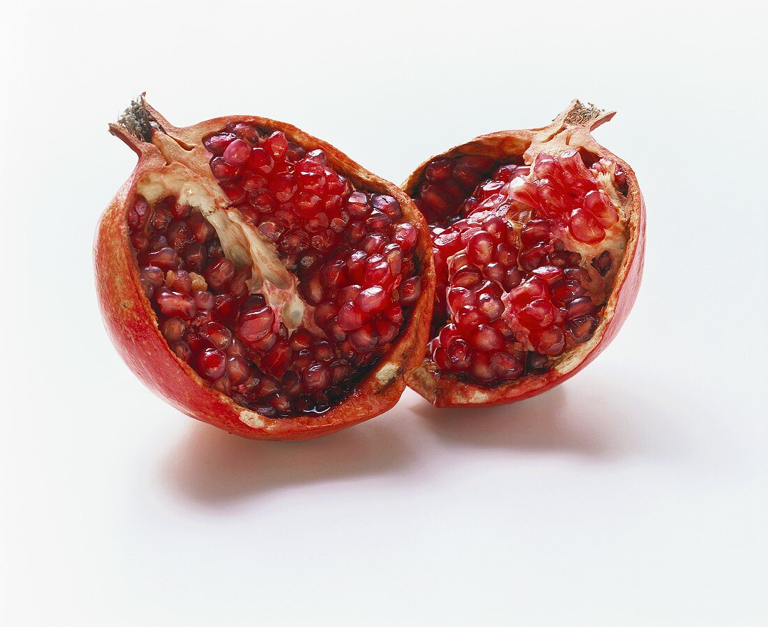 Two pomegranate halves with seeds on white background