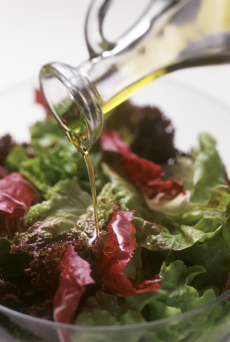 Öl aus Glaskaraffe auf gemischten Salat gießen