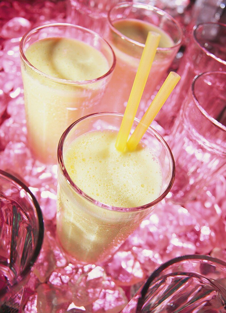 Three milkshakes among pink ice cubes and glasses