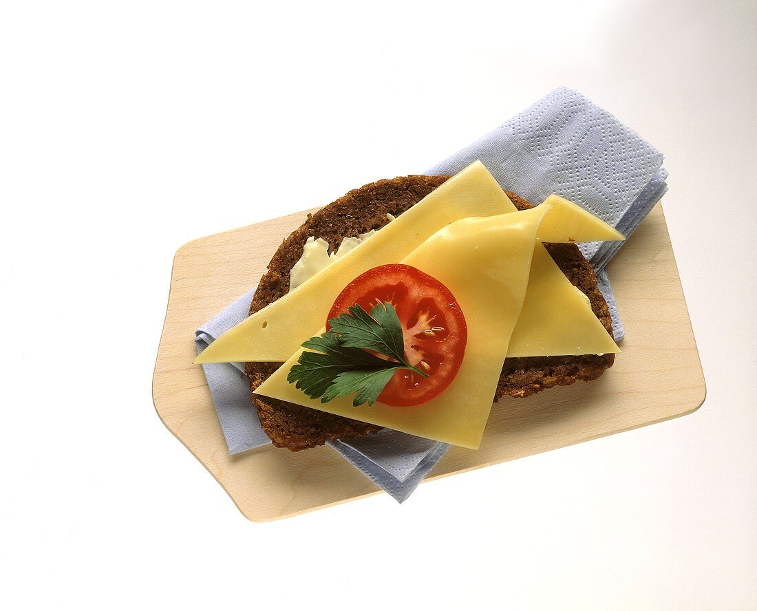 Wholemeal bread topped with cheese & tomato on wooden board