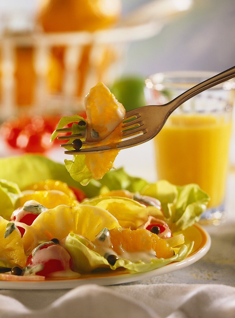 Salat mit Ananas, Orangen & Tomaten auf Teller & Gabel