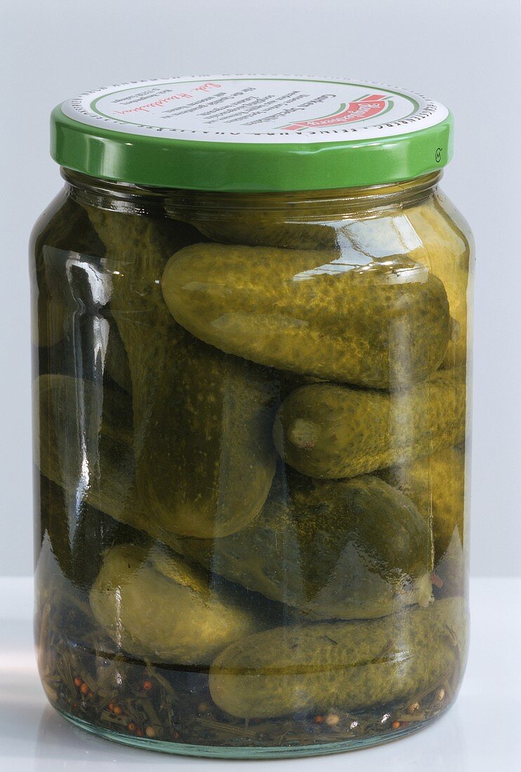 Pickled gherkins in jar on light background