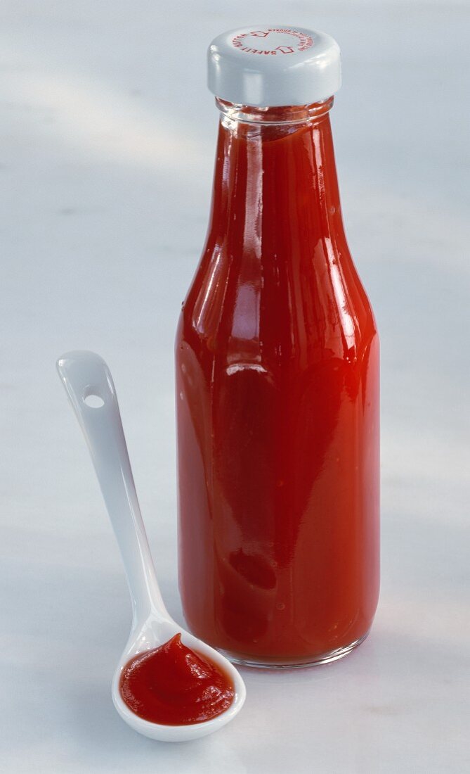 Tomatenketchup in einer Flasche & daneben auf weißem Löffel