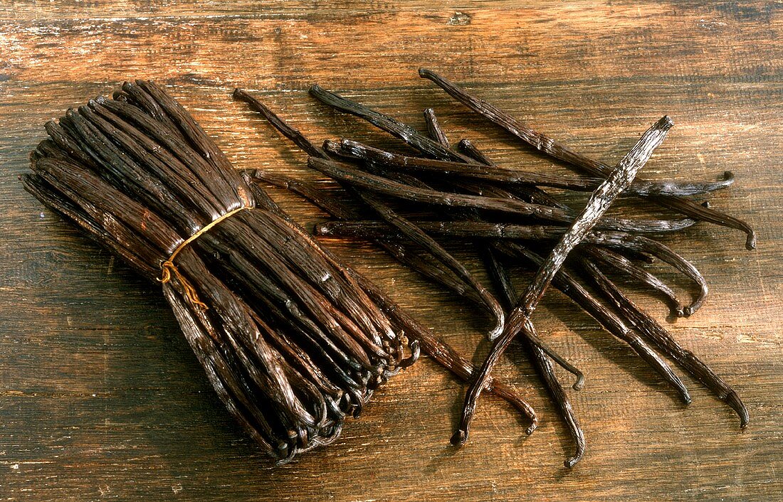 Vanilla pods, tied together & singly on wooden background