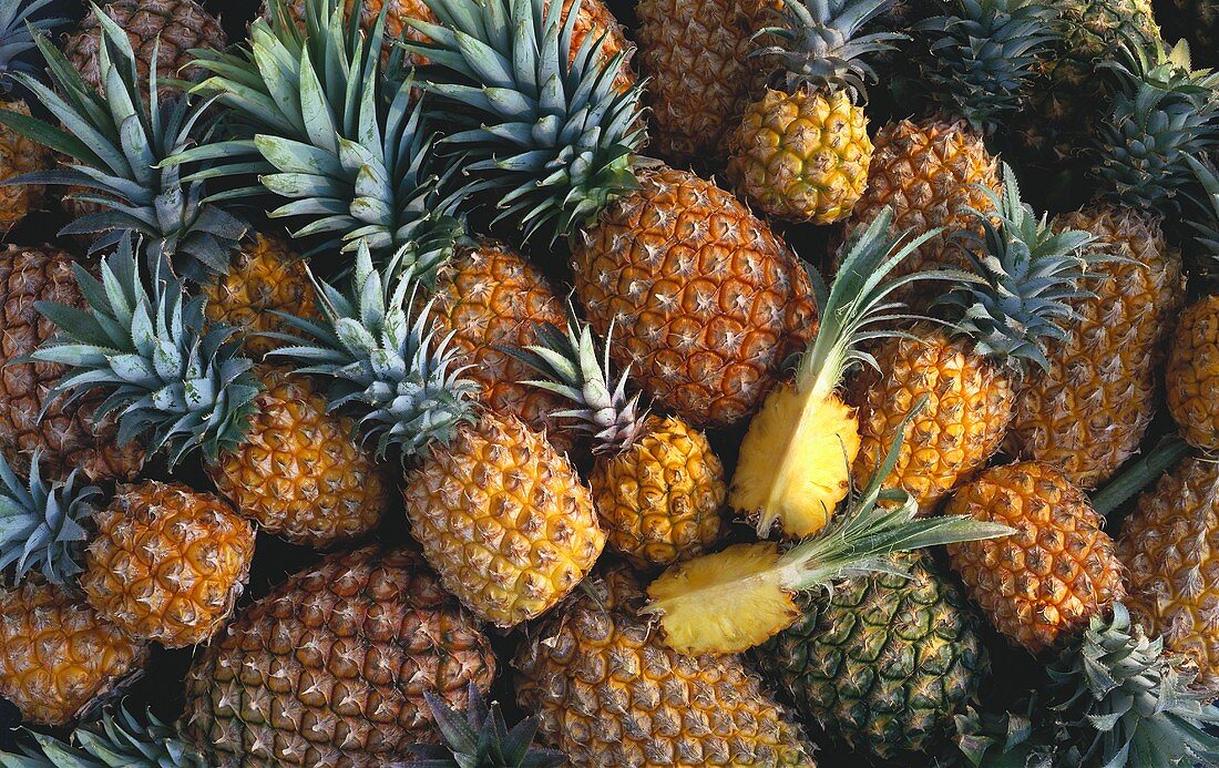 Many whole pineapples, two pineapple quarters (close-up)