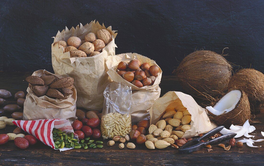Nuts in various paper bags & coconuts on wooden background