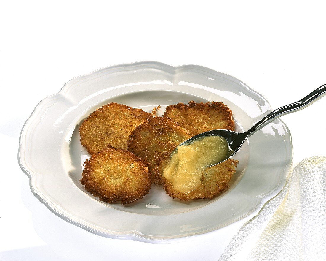 Kartoffelpuffer auf weißem Teller und Apfelmus auf Löffel