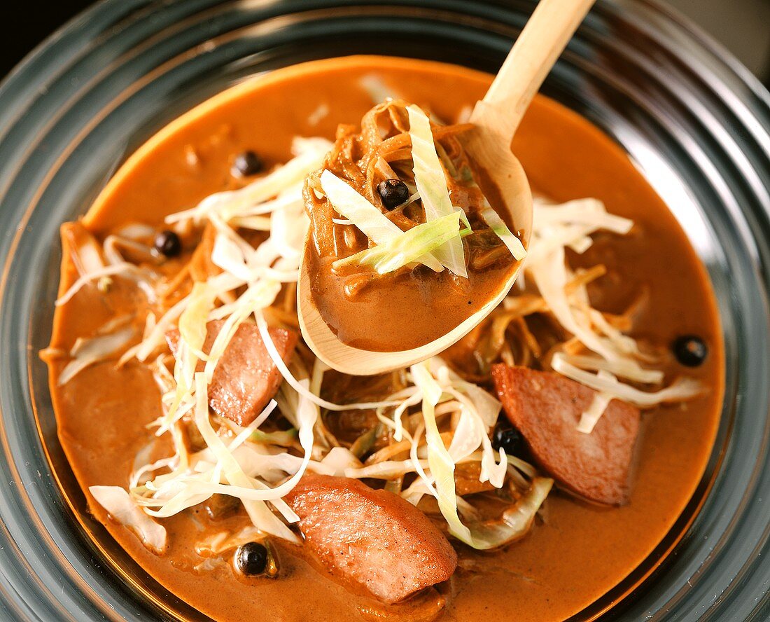 Ungarische Krautsuppe mit Wurst auf Teller und Löffel