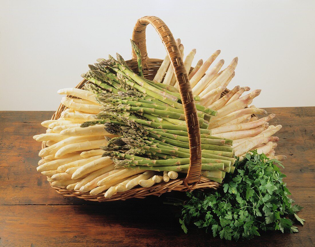 White and green asparagus in a basket, with parsley in front