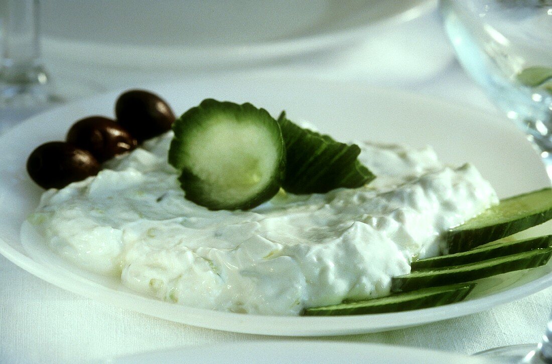 Tzaziki mit Gurkenscheiben und Oliven auf weißem Teller