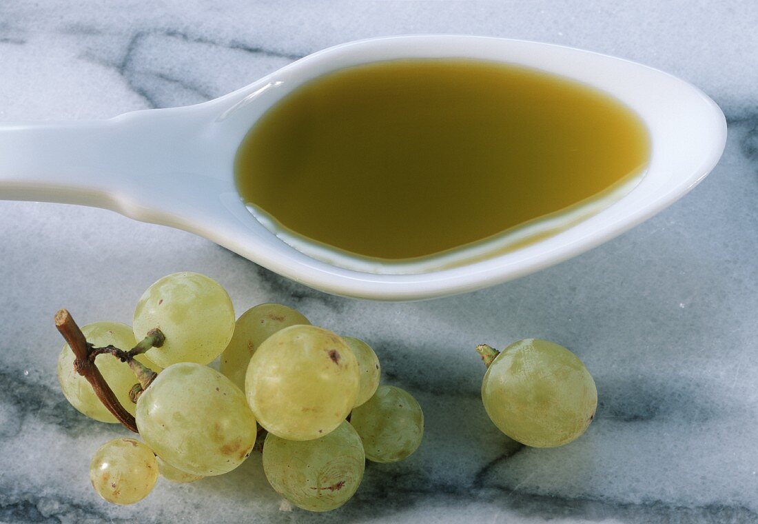 Grape seed oil on spoon beside green grapes on marble
