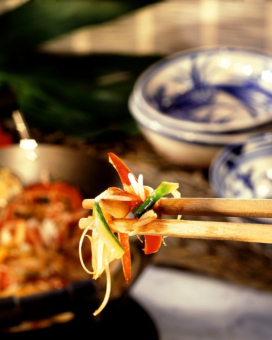 Vegetables with rice on chopsticks with wok & Asian bowls