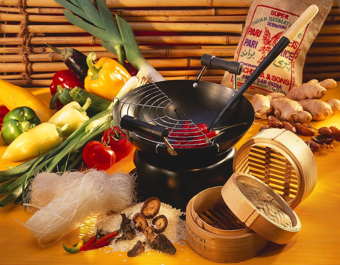 Still life with wok, bamboo steamer, vegetables, noodles, rice